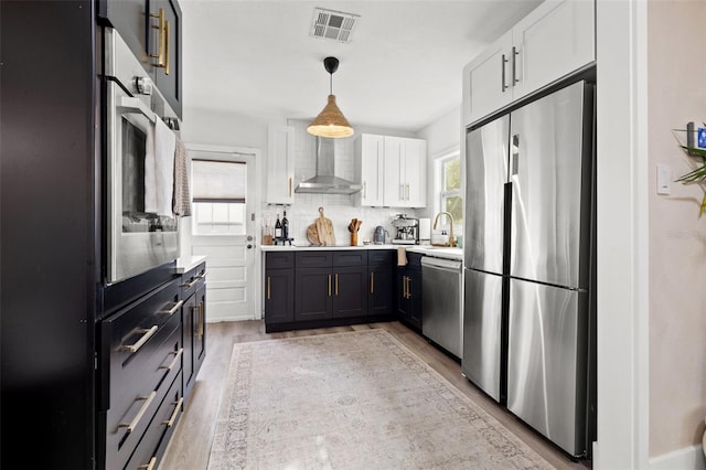 kitchen featuring wall chimney exhaust hood, sink, white cabinetry, hanging light fixtures, and appliances with stainless steel finishes