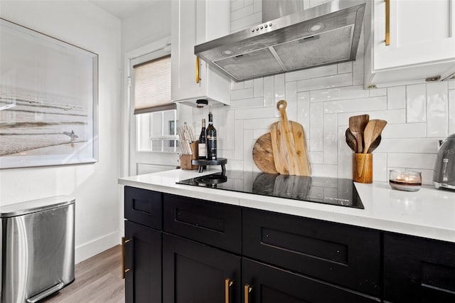 kitchen featuring tasteful backsplash, light wood-type flooring, black electric cooktop, wall chimney range hood, and white cabinets