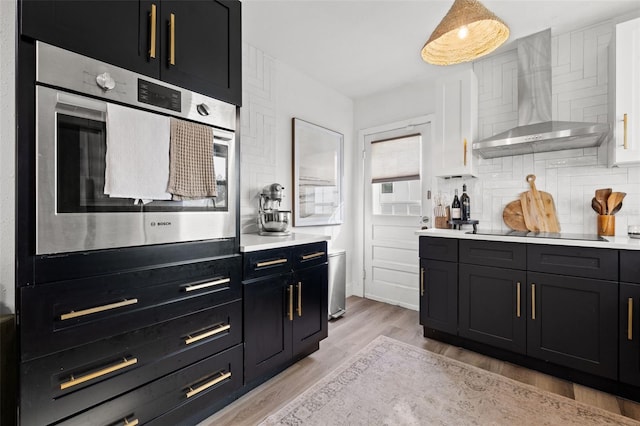 kitchen featuring stainless steel oven, wall chimney range hood, black electric stovetop, light hardwood / wood-style floors, and backsplash