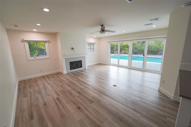 unfurnished living room featuring ceiling fan, a tiled fireplace, and light wood-type flooring