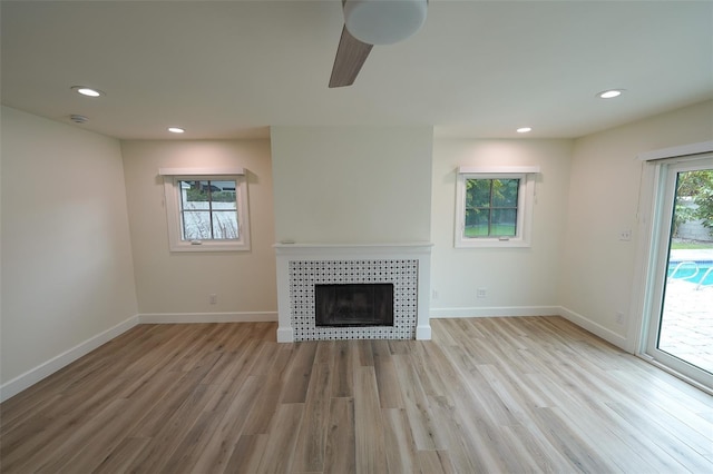 unfurnished living room with a tile fireplace, ceiling fan, and light wood-type flooring