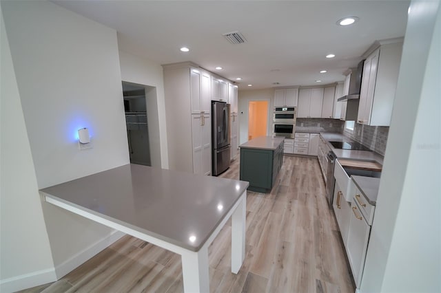 kitchen with appliances with stainless steel finishes, white cabinets, decorative backsplash, a center island, and light hardwood / wood-style floors