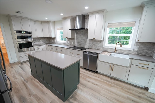 kitchen featuring wall chimney exhaust hood, sink, a center island, stainless steel appliances, and white cabinets