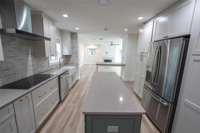 kitchen with a kitchen island, tasteful backsplash, stainless steel appliances, wall chimney range hood, and light wood-type flooring