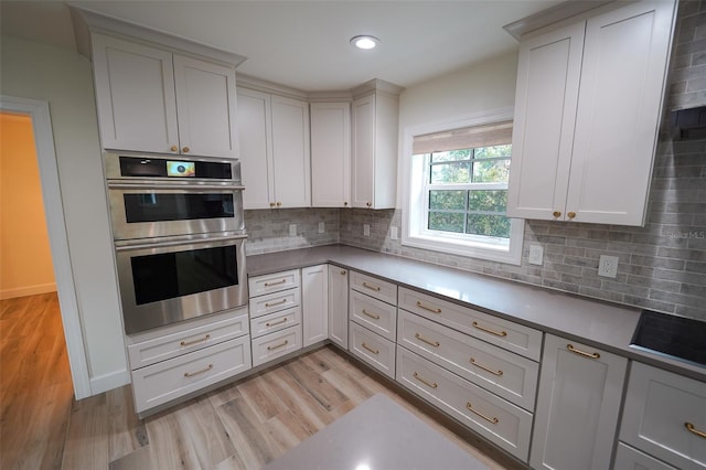 kitchen featuring stainless steel double oven, light hardwood / wood-style floors, and decorative backsplash