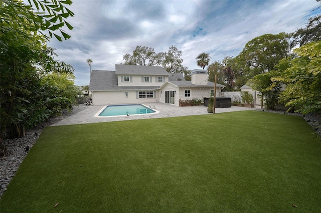 back of property with a swimming pool with hot tub, a patio area, and a lawn