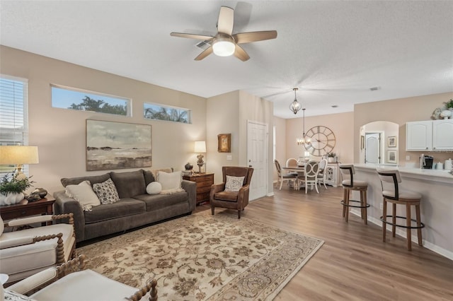 living room with a textured ceiling, light hardwood / wood-style floors, and ceiling fan with notable chandelier