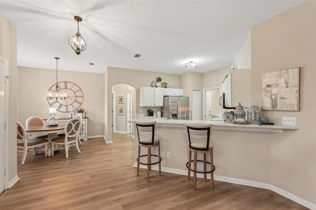 kitchen with kitchen peninsula, white cabinetry, stainless steel fridge, and hanging light fixtures