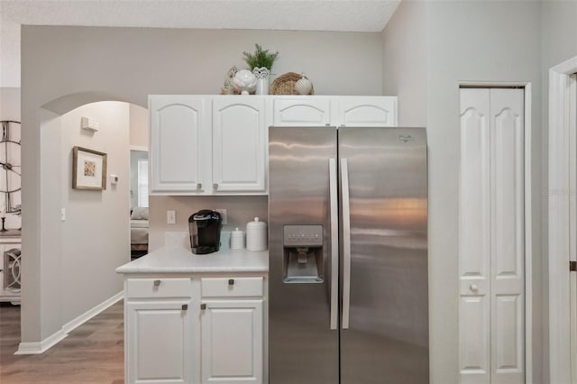 kitchen with a textured ceiling, hardwood / wood-style floors, stainless steel refrigerator with ice dispenser, and white cabinetry