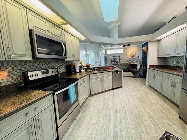 kitchen featuring a fireplace, dark stone counters, sink, pendant lighting, and stainless steel appliances