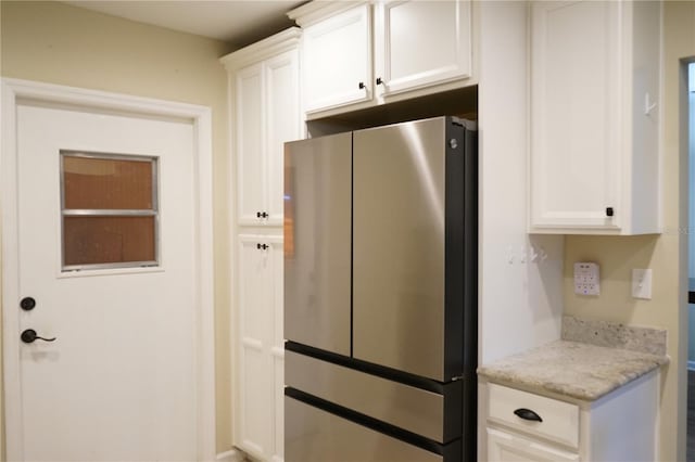 kitchen with light stone counters, stainless steel fridge, and white cabinets