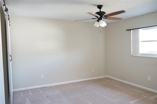 spare room with ceiling fan, a barn door, light carpet, and a textured ceiling