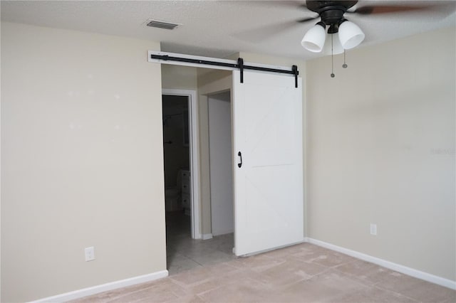 spare room with light carpet, a textured ceiling, a barn door, and ceiling fan