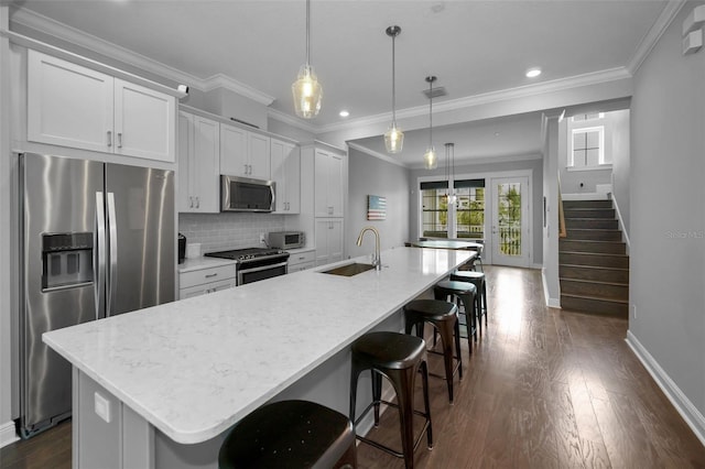 kitchen featuring an island with sink, white cabinetry, sink, hanging light fixtures, and stainless steel appliances