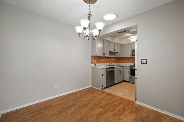 kitchen featuring pendant lighting, appliances with stainless steel finishes, a textured ceiling, sink, and light hardwood / wood-style flooring