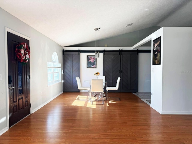 interior space featuring vaulted ceiling, a barn door, and wood-type flooring