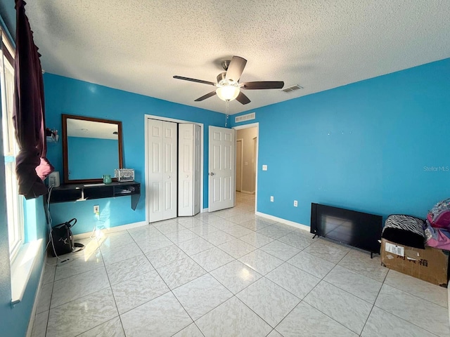 unfurnished bedroom with ceiling fan, a closet, a textured ceiling, and light tile patterned flooring