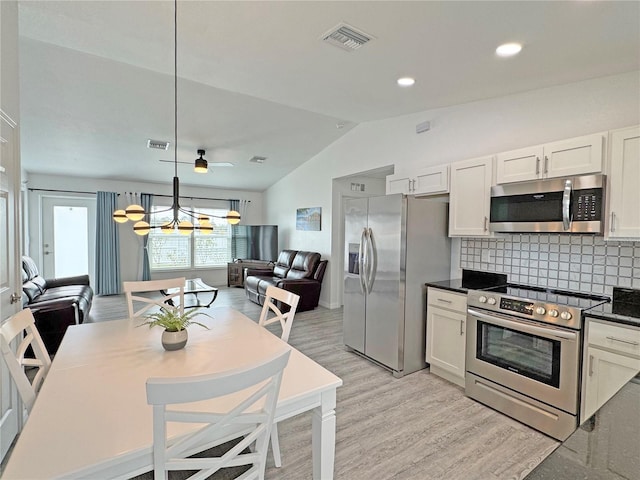 kitchen with appliances with stainless steel finishes, pendant lighting, white cabinetry, lofted ceiling, and backsplash