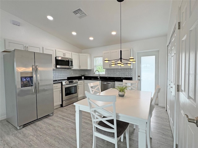 kitchen featuring pendant lighting, lofted ceiling, white cabinetry, backsplash, and stainless steel appliances