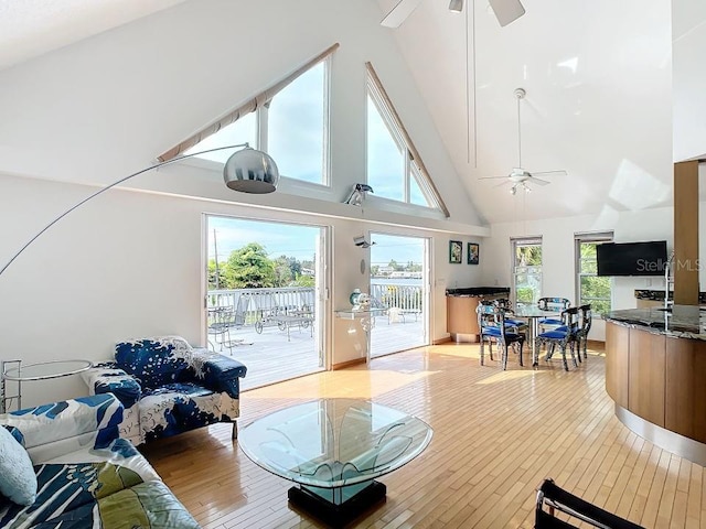 living room with high vaulted ceiling, ceiling fan, and light hardwood / wood-style flooring