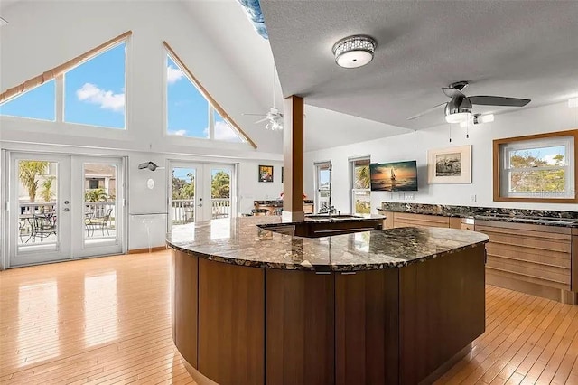 kitchen featuring french doors, light hardwood / wood-style flooring, stainless steel gas stovetop, ceiling fan, and dark stone counters