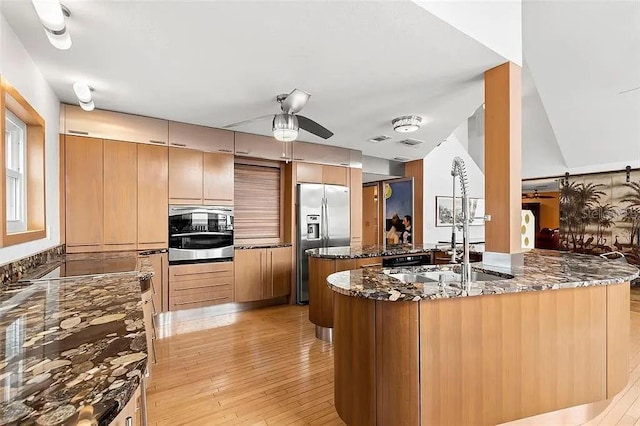 kitchen featuring ceiling fan, dark stone countertops, stainless steel appliances, kitchen peninsula, and light wood-type flooring