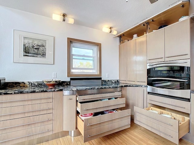 kitchen with dark stone countertops, oven, a textured ceiling, and light hardwood / wood-style flooring