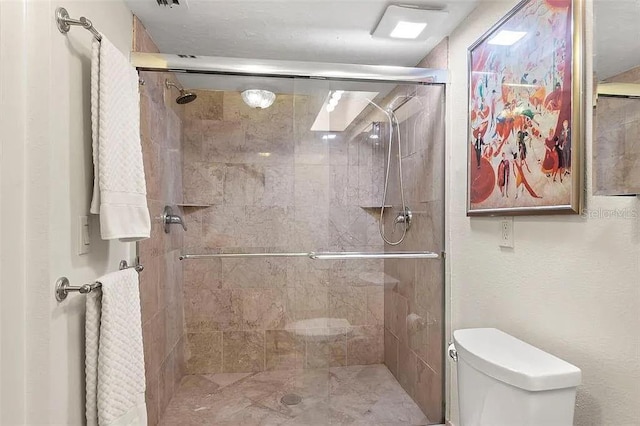 bathroom featuring a shower with door and toilet