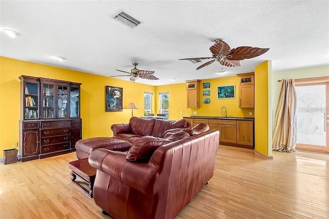 living room featuring sink, a textured ceiling, ceiling fan, and light wood-type flooring