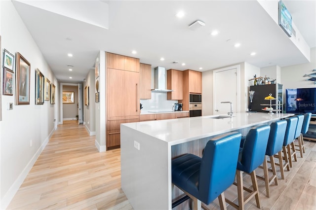 kitchen featuring a breakfast bar, sink, wall chimney exhaust hood, black appliances, and a spacious island