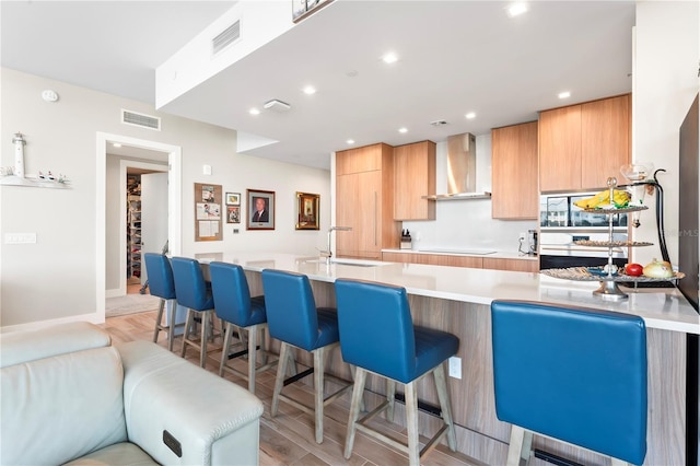 kitchen featuring a breakfast bar, electric stovetop, sink, wall chimney range hood, and light hardwood / wood-style flooring