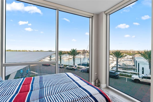 bedroom featuring multiple windows, hardwood / wood-style floors, floor to ceiling windows, and a water view