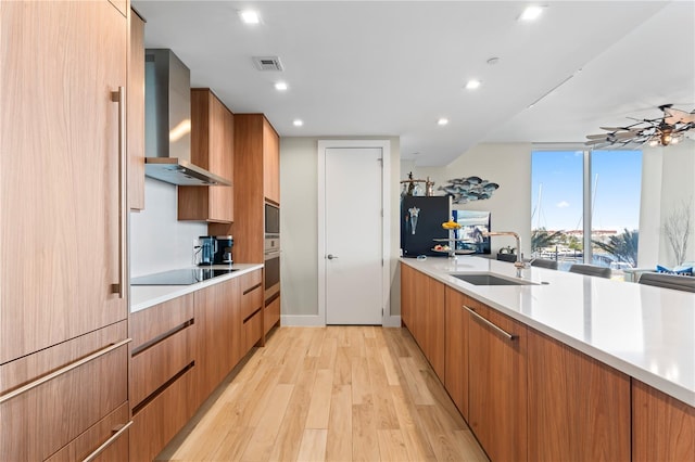 kitchen with sink, floor to ceiling windows, black electric stovetop, wall chimney exhaust hood, and light wood-type flooring