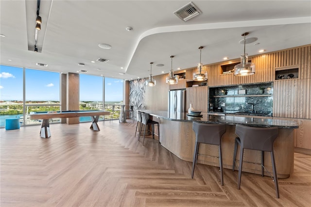 kitchen with dark stone countertops, decorative light fixtures, stainless steel refrigerator, and light parquet floors