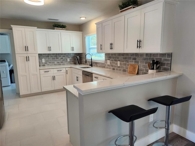 kitchen featuring light stone counters, a peninsula, a sink, white cabinets, and washer / dryer