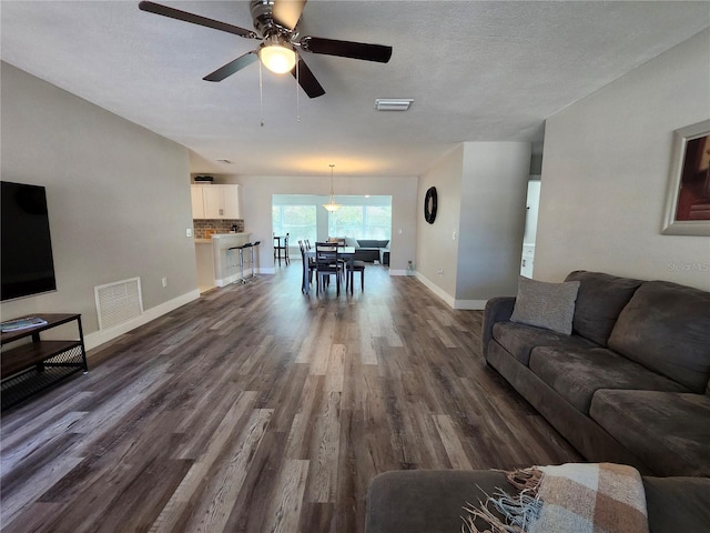 living area with a textured ceiling, dark wood finished floors, visible vents, and baseboards