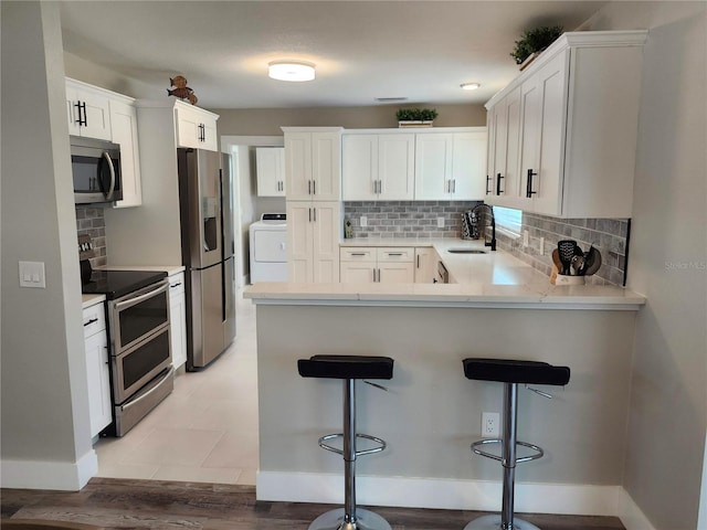 kitchen featuring backsplash, appliances with stainless steel finishes, a sink, washer / dryer, and a peninsula