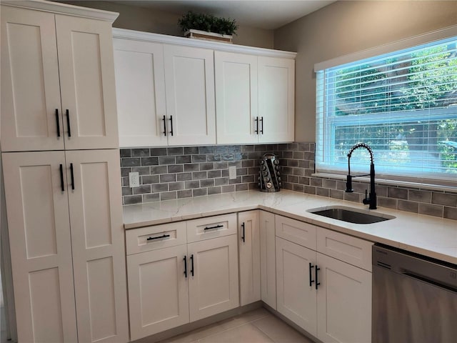 kitchen featuring light tile patterned floors, a sink, white cabinetry, stainless steel dishwasher, and tasteful backsplash