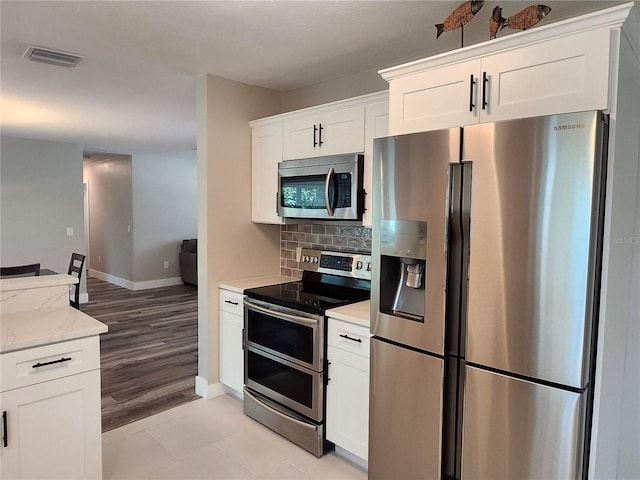 kitchen with light stone counters, visible vents, decorative backsplash, appliances with stainless steel finishes, and white cabinets