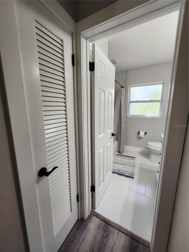 full bath featuring toilet, curtained shower, and wood finished floors