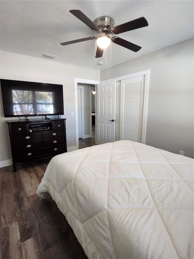 bedroom featuring dark wood-style flooring, visible vents, baseboards, a ceiling fan, and a closet