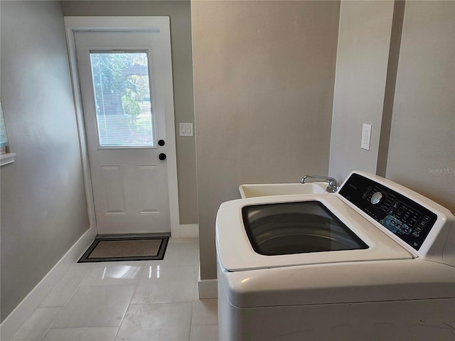 clothes washing area featuring washer / dryer, laundry area, baseboards, tile patterned flooring, and a sink