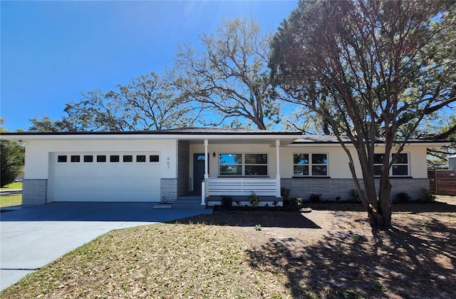 ranch-style home featuring brick siding, stucco siding, covered porch, a garage, and driveway