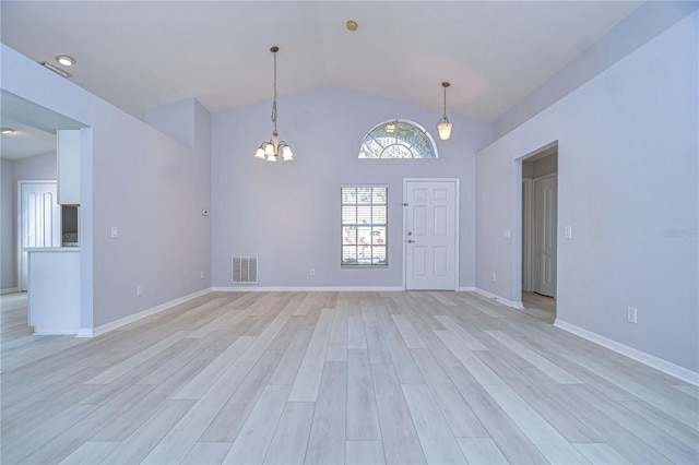 spare room with lofted ceiling, a chandelier, visible vents, baseboards, and light wood-style floors