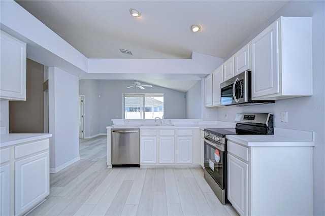 kitchen featuring stainless steel appliances, a peninsula, a sink, vaulted ceiling, and light countertops