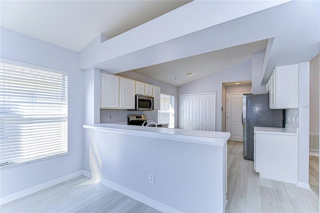 kitchen featuring lofted ceiling, white cabinetry, stainless steel appliances, and light countertops