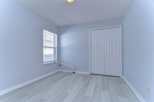 unfurnished bedroom with light wood-type flooring, a closet, and baseboards