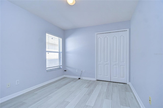 unfurnished bedroom with light wood-style floors, baseboards, and a closet