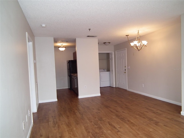 unfurnished living room featuring dark hardwood / wood-style flooring, washer / dryer, a textured ceiling, and a notable chandelier