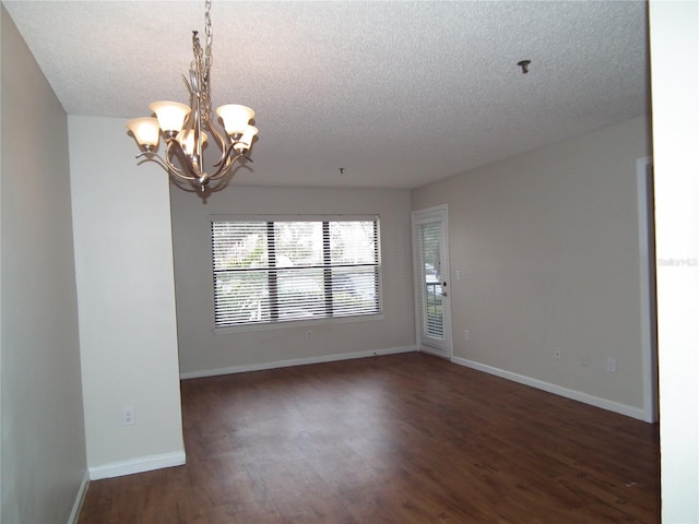 spare room featuring a notable chandelier, dark wood-type flooring, and a textured ceiling